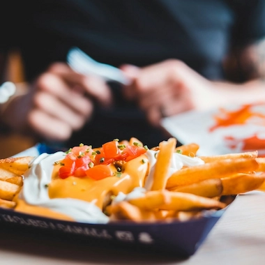 Fries covered in sour cream, cheese, and tomatoes in a black basket.