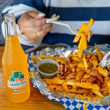 A person eating fries with cheese and bacon with an orange soda.