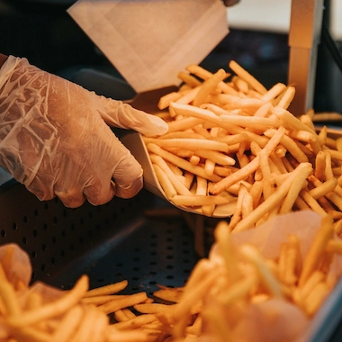 A person scooping fries into a paper bag.