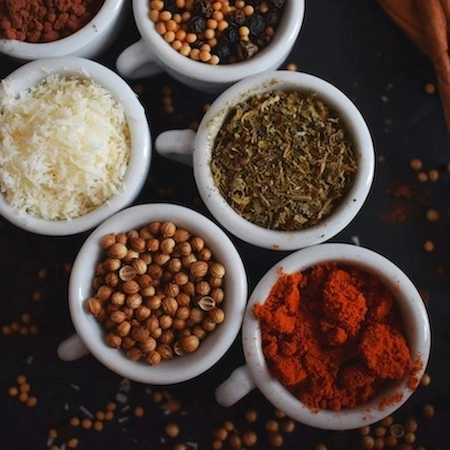 various colourful spices in white mugs lined up beside each other.